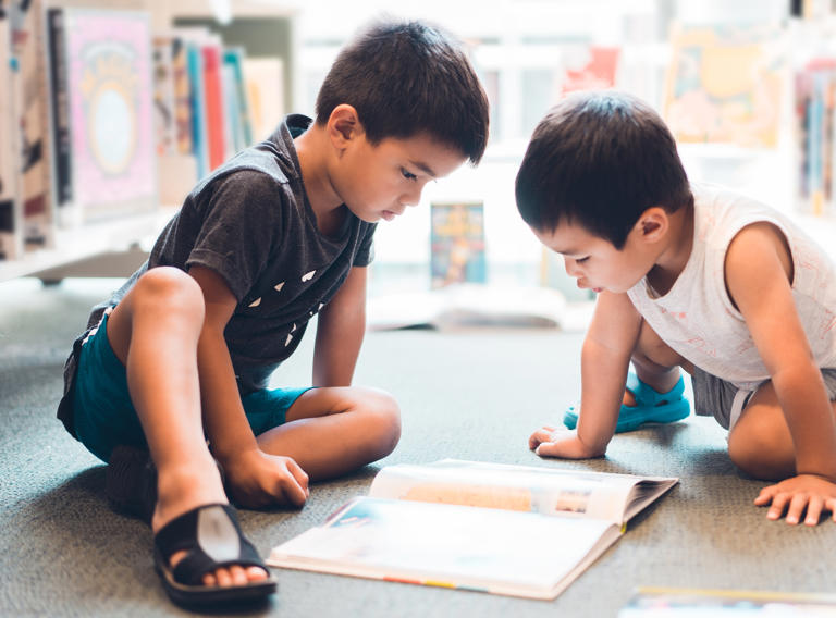 Two young boys reading a book in the library